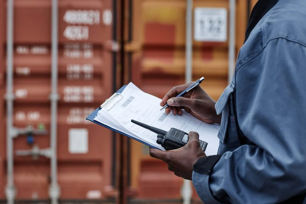 Logistics officer with clipboard, paperwork, and walkie-talkie near shipping containers